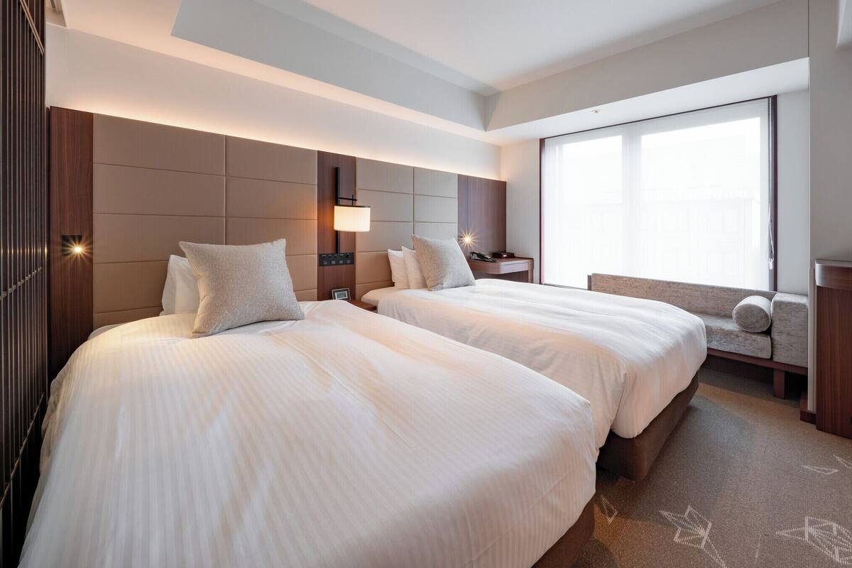 Une chambre d’hôtel avec deux lits, une grande fenêtre et un téléviseur.
