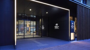 Une entrée d’hôtel moderne avec des portes en verre, un éclairage décoratif et une vue dégagée sur le hall d’accueil.