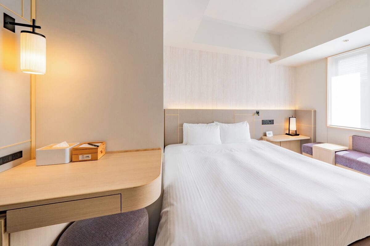 Une chambre d’hôtel avec un grand lit, des tables de chevet, une lampe, une fenêtre et un coin salon.