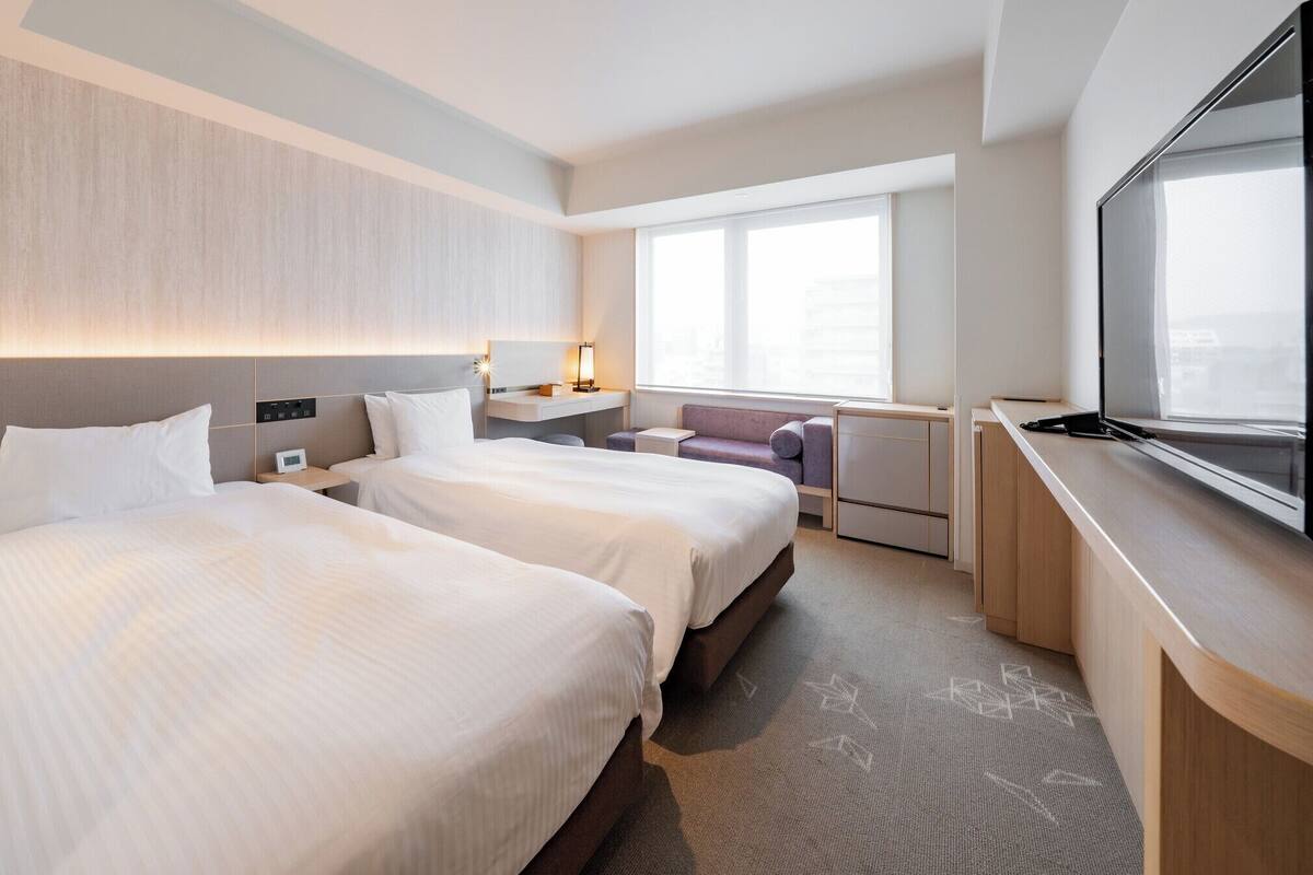 Une chambre d’hôtel avec deux lits, un bureau, une chaise, une télévision et une fenêtre.