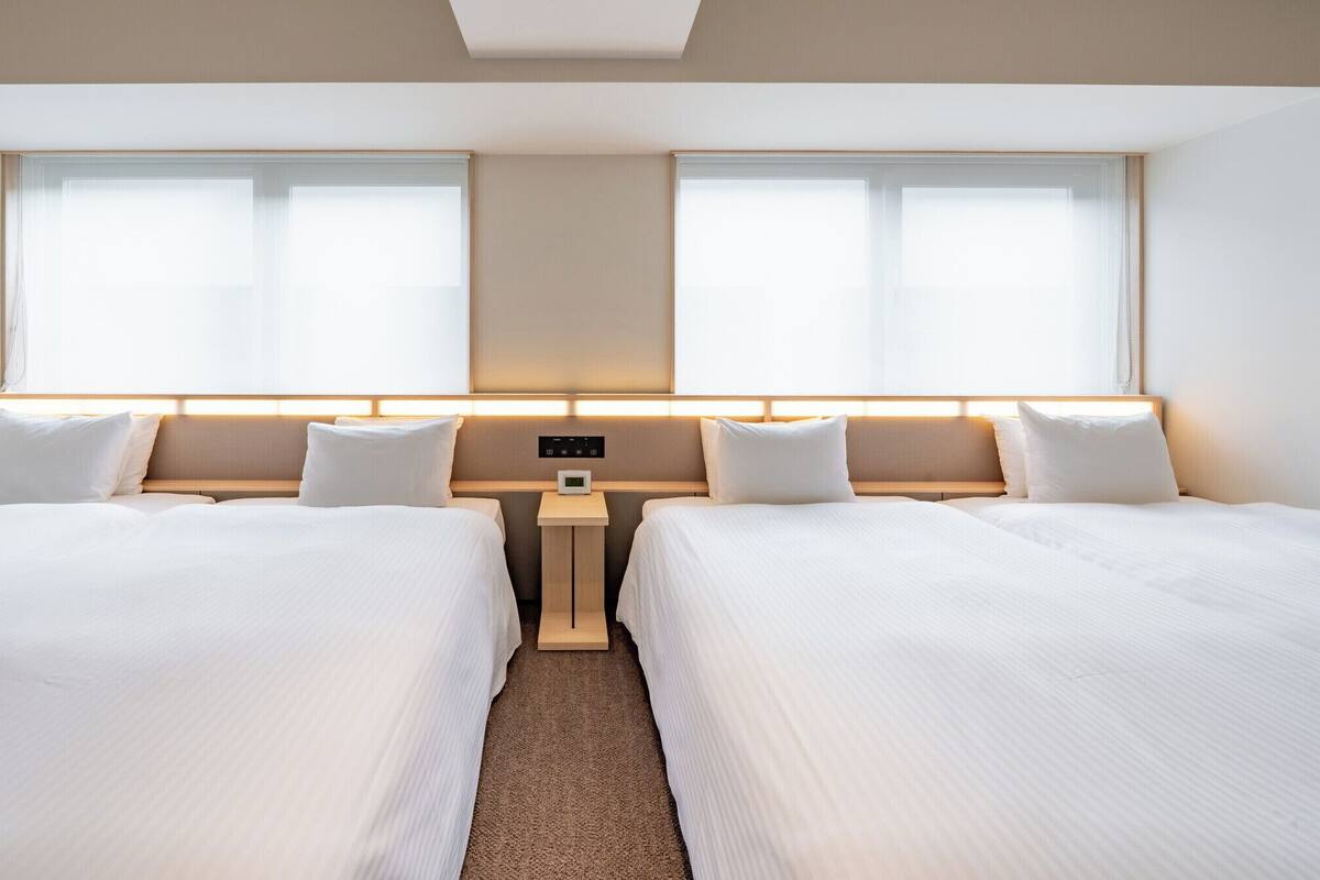 Une chambre d’hôtel avec deux lits, une table de chevet et un panneau de commande.