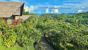 A thatched-roof building with a wooden balcony overlooking a lush, green landscape and a distant view of the sea. - Palau Carolines Resort (Meyungs)