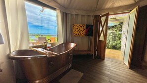 A room with a wooden floor, a bathtub, a window with curtains, and a view of the sea. - Palau Carolines Resort (Meyungs)