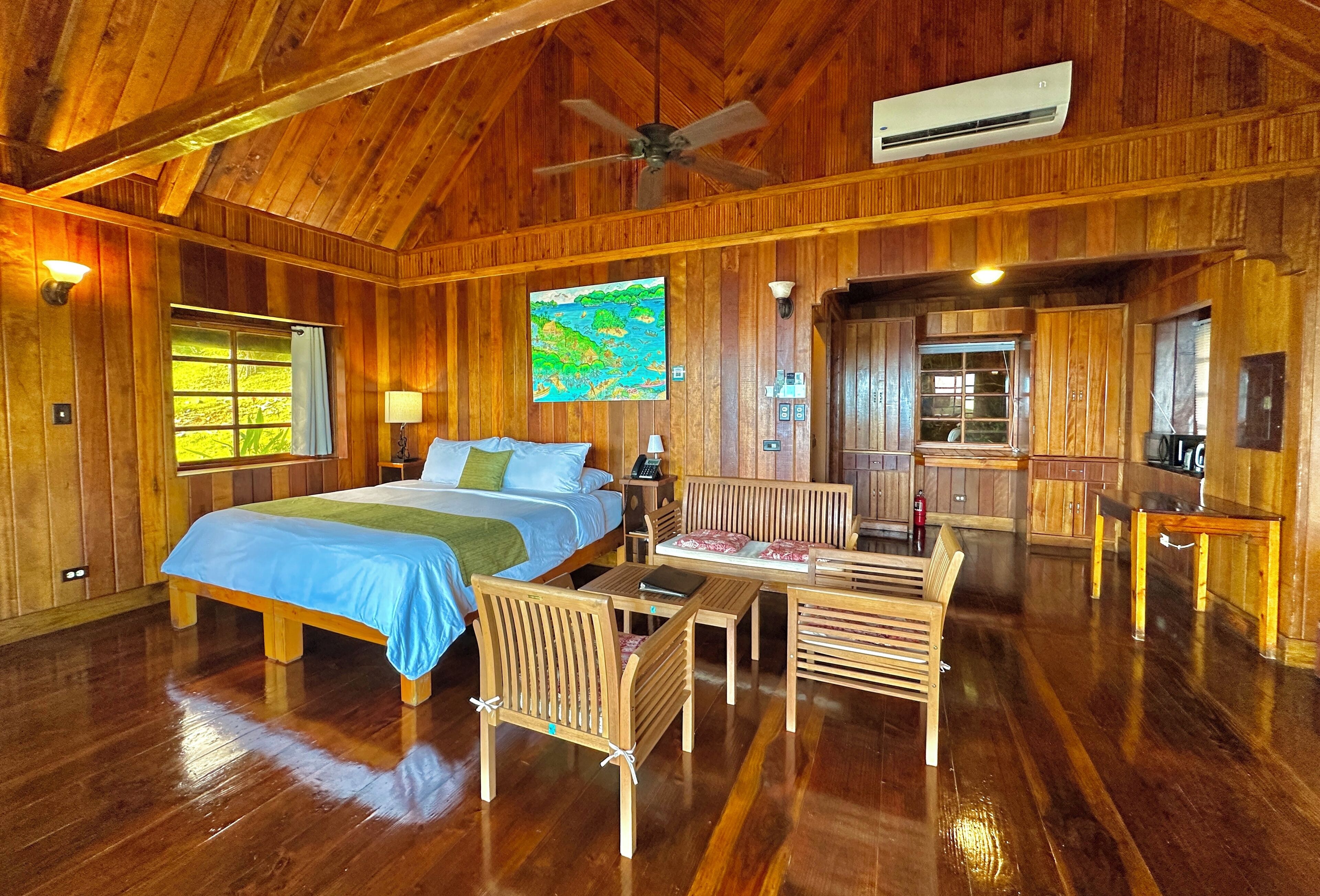 A wooden cabin with a large bed, a dining table, and a kitchen area.