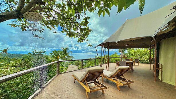 A wooden deck with two lounge chairs, a table, and a canopy. - Palau Carolines Resort (Meyungs)