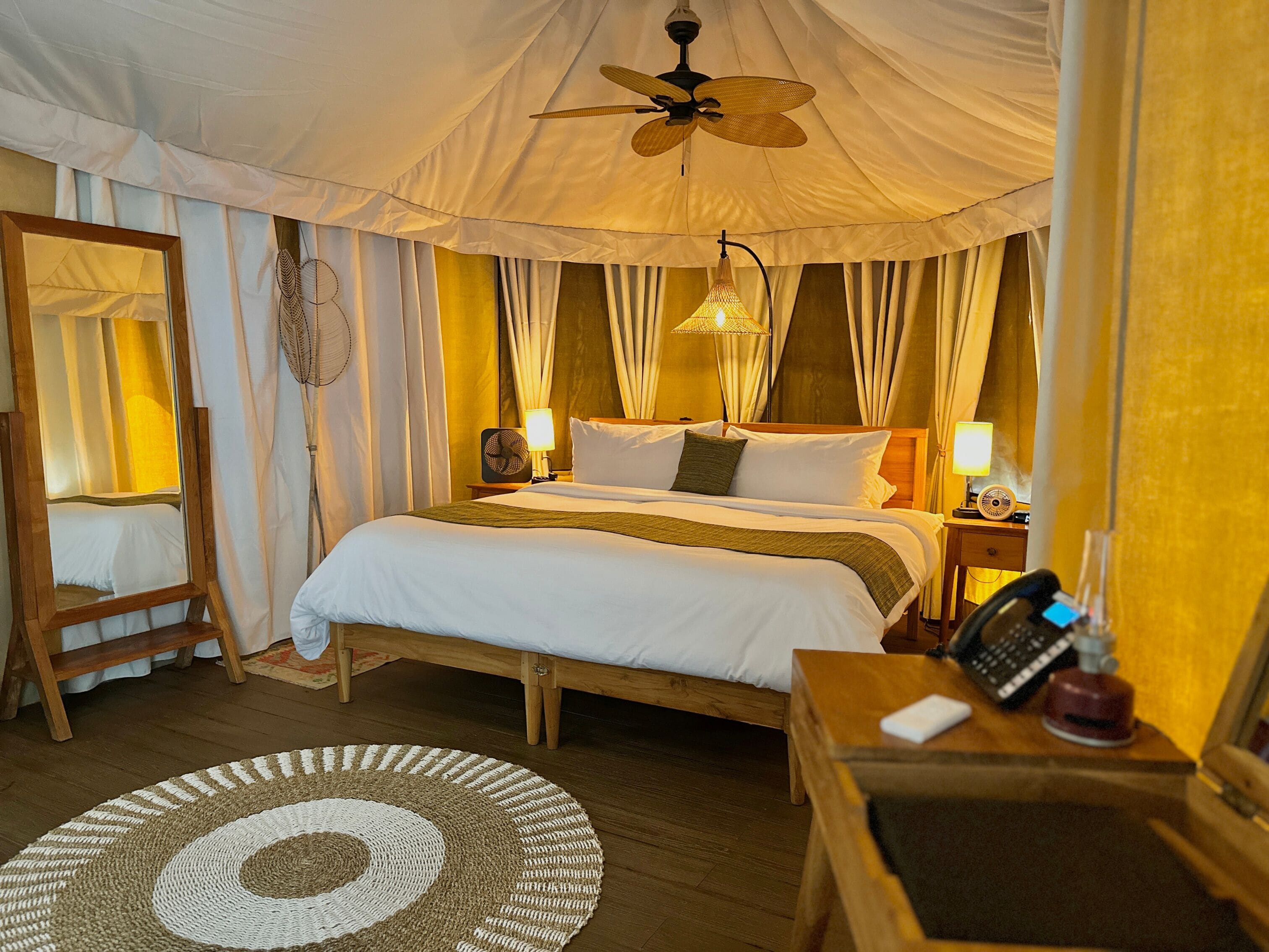Une chambre confortable avec un lit, des lampes de chevet, un ventilateur de plafond, une table de chevet en bois et un miroir.