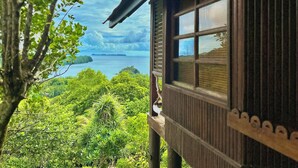 A wooden cabin with a large window overlooking a lush landscape and a body of water. - Palau Carolines Resort (Meyungs)