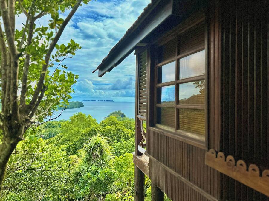A wooden cabin with a large window overlooking a lush landscape and a body of water.