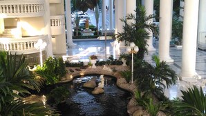 A hotel lobby with a central water feature, columns, and a balcony with railings. - Sky Beach Apartment (Pattaya)
