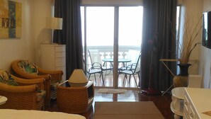 A hotel room with a large bed, a desk, a chair, a small table, a lamp, a potted plant, and a view of the balcony and outside. - Sky Beach Apartment (Pattaya)