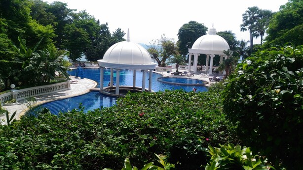 A pool area with two white domed structures, surrounded by lush greenery. - Sky Beach Apartment (Pattaya)