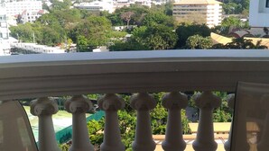 A balcony with a round glass table and a chair, overlooking a cityscape with buildings and greenery. - Sky Beach Apartment (Pattaya)