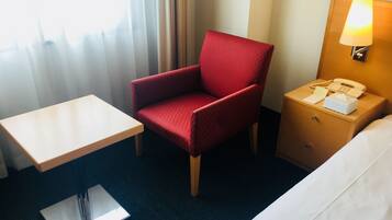 Habitación de hotel con un sillón rojo, una mesita, una mesita de noche con lámpara y una cama.