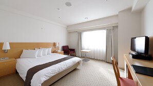 Une chambre d’hôtel avec un grand lit, un bureau avec une télévision, une chaise, une table de chevet et une fenêtre avec des rideaux.