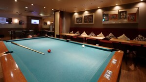 Une table de billard avec une boule rouge et un bâton, entourée de tables et de chaises.