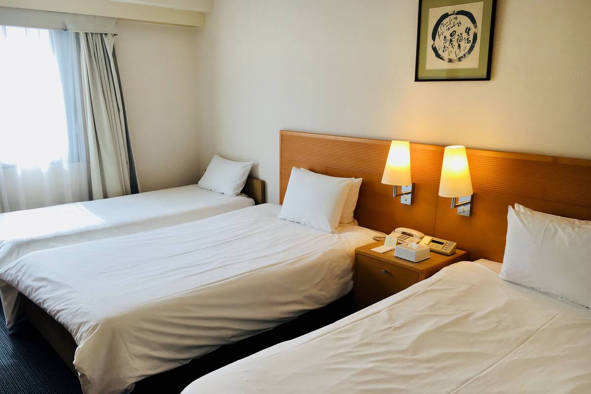 A hotel room with two single beds, a bedside table with a lamp, a phone, and a framed picture on the wall.