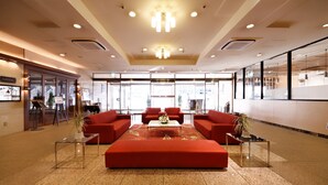 Un hall d’entrée spacieux, avec un ensemble de canapés rouges, une table basse en verre et un lustre.