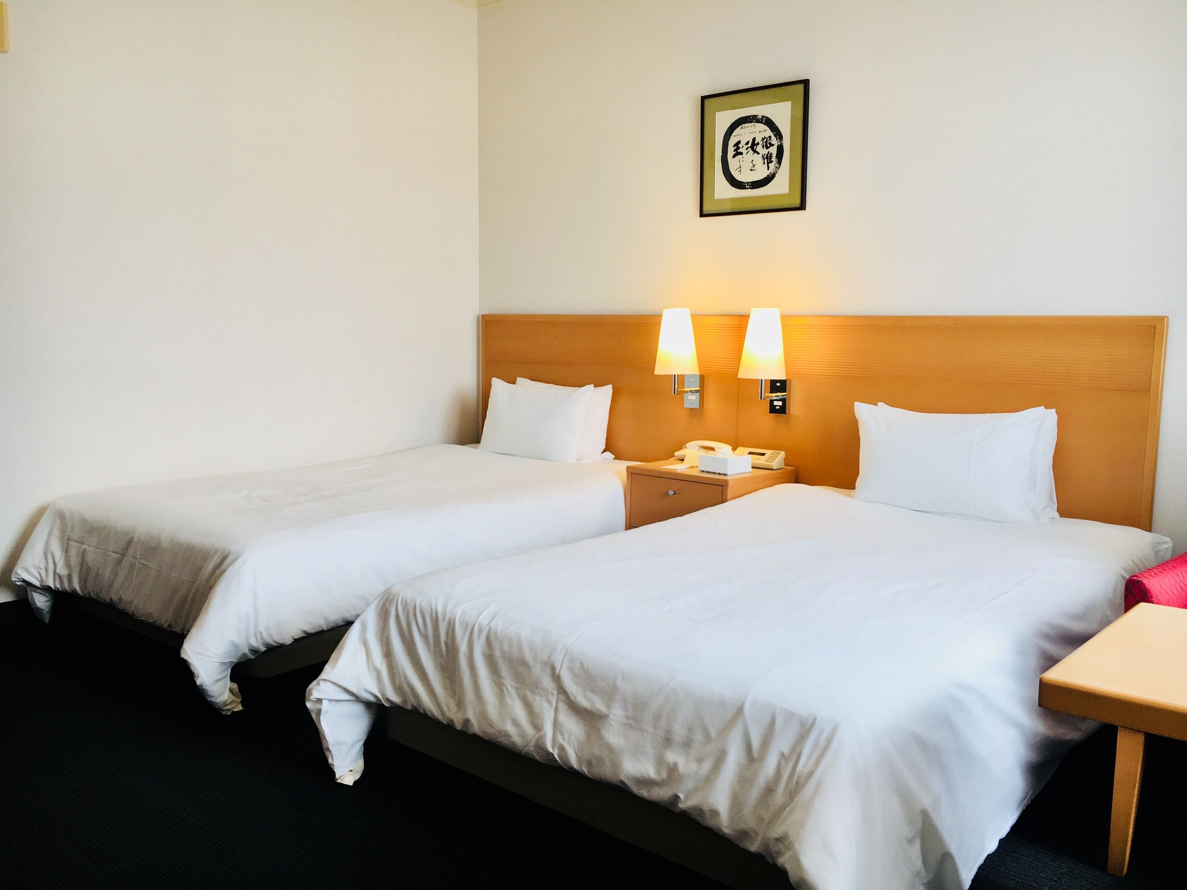 Habitación de hotel con dos camas, una mesita de noche con teléfono y un cuadro enmarcado en la pared.