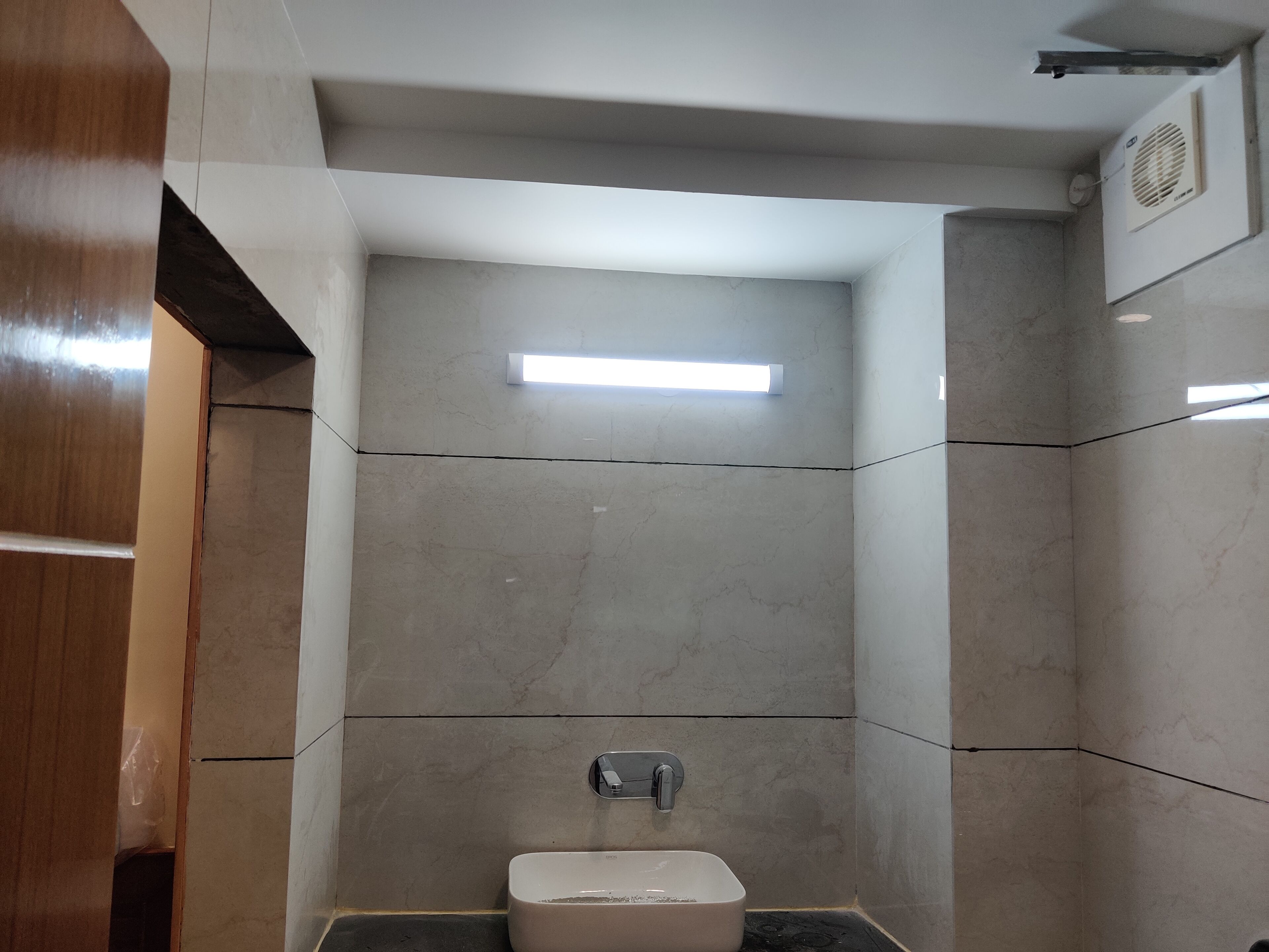 Et lille, moderne badeværelse med toilet, vægmonteret håndvask og ventilation i loftet.