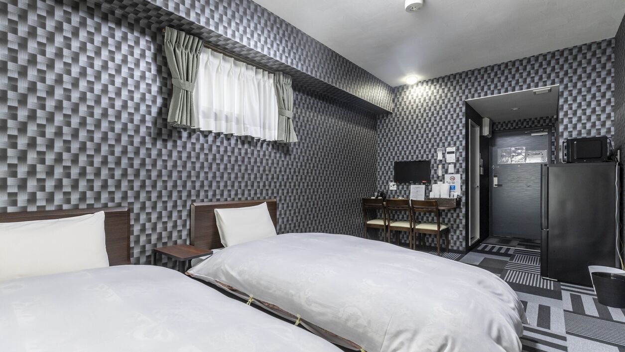 Quarto de hotel com padrão de parede quadriculado, uma cama com roupa de cama branca, uma escrivaninha com cadeira, uma televisão e um frigorífico.