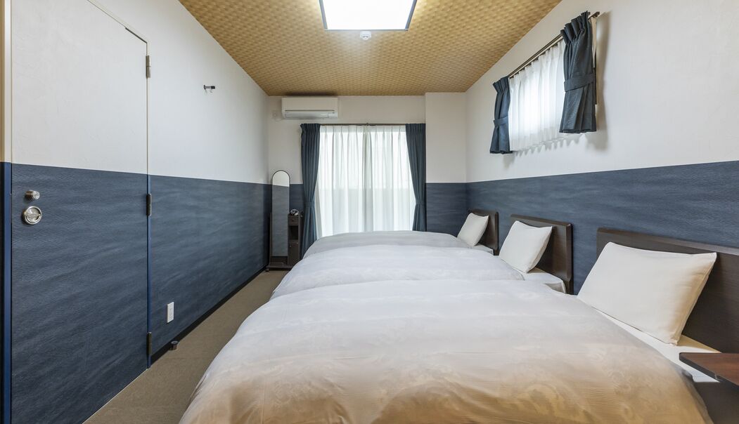 Quarto de hotel com uma cama grande, um guarda-roupa, um espelho e uma janela com cortinas.