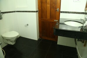 A bathroom with a toilet, a wooden door, a sink, and black tiled flooring. - Travancore Island Resort (Thiruvananthapuram)