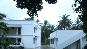 A white building with a car parked in front and a motorcycle parked to the side. - Travancore Island Resort (Thiruvananthapuram)