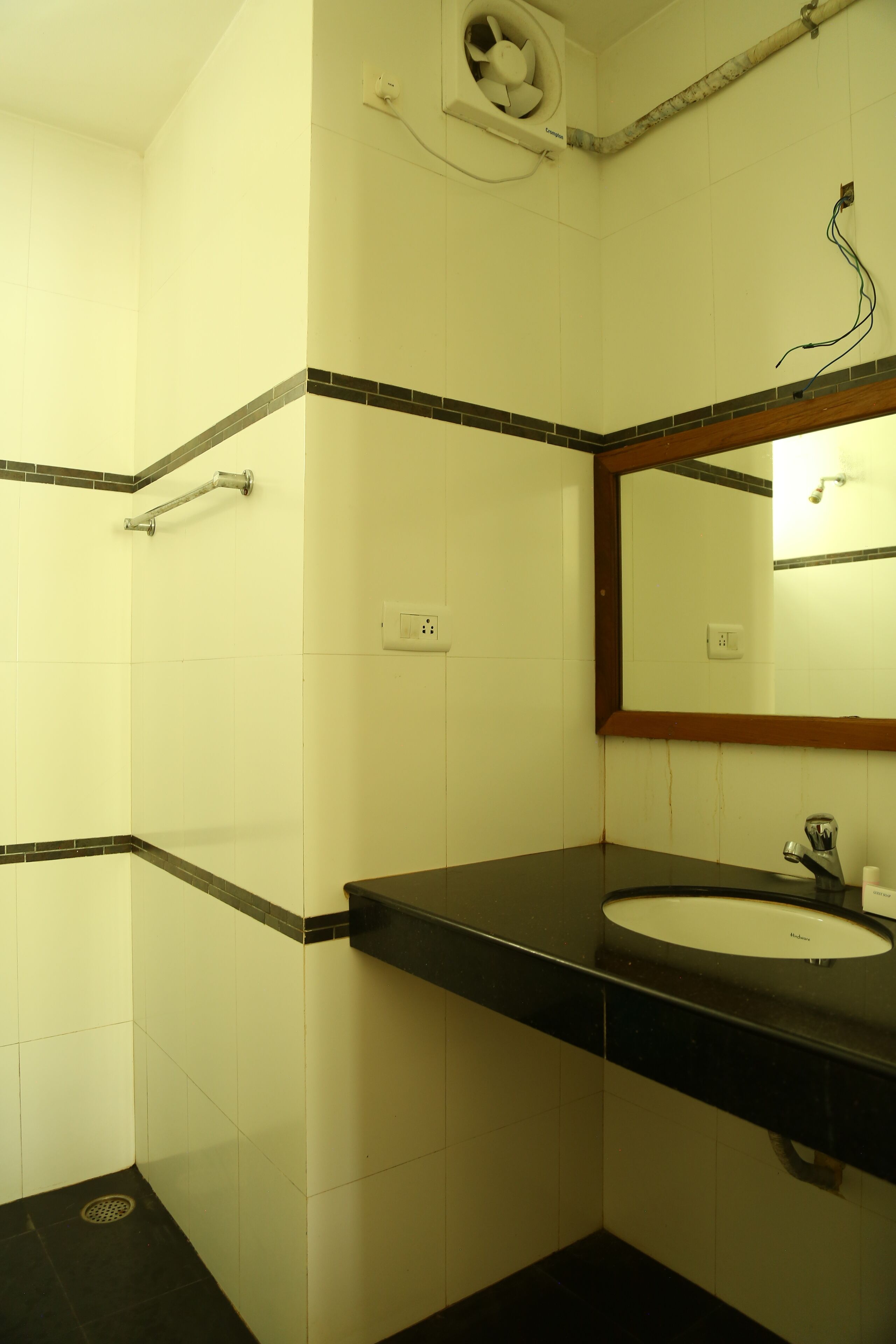 Un baño con lavamanos blanco, encimera negra y un espejo con marco de madera.