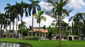 A well-maintained garden with a pond, palm trees, and a building with a red roof. - Rinn Boutique House (Chiang Mai)