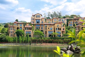 Un hôtel à plusieurs étages, de style architectural méditerranéen, doté d’une cour intérieure et offrant une vue sur un lac.