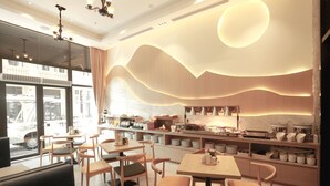 Un intérieur de restaurant moderne, avec des meubles en bois, un espace cuisine et une vue sur la rue grâce à de grandes fenêtres.