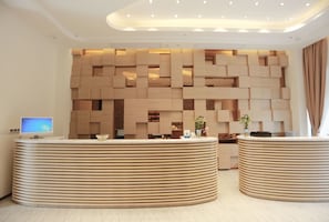 A modern reception area with a wooden wall design, two curved reception desks, and a computer monitor on the left. - Poltton International Service Apartment Mayangxi Branch (Zhangzhou)