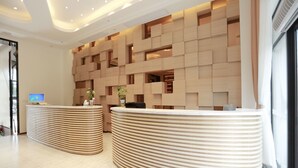Un espace d’accueil doté de deux comptoirs d’accueil incurvés, d’un design mural moderne avec des luminaires encastrés et d’une grande fenêtre sur le côté droit.