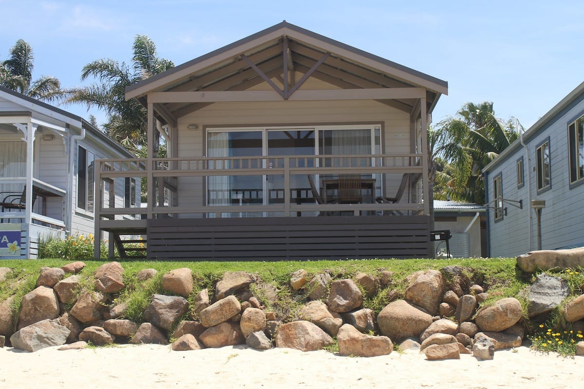Una casa frente a la playa con porche cubierto, ventanas amplias y un muro de piedra.