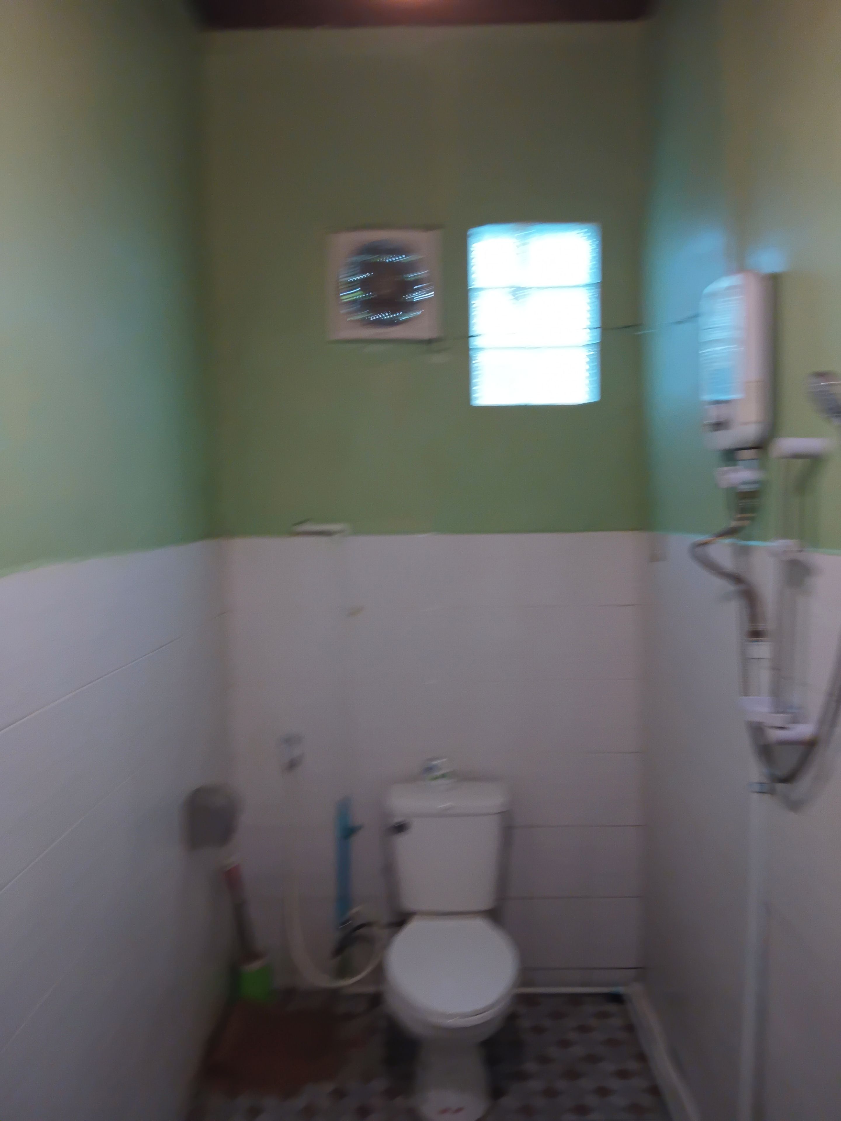 A small bathroom with a toilet, a window, and a wall-mounted heater.