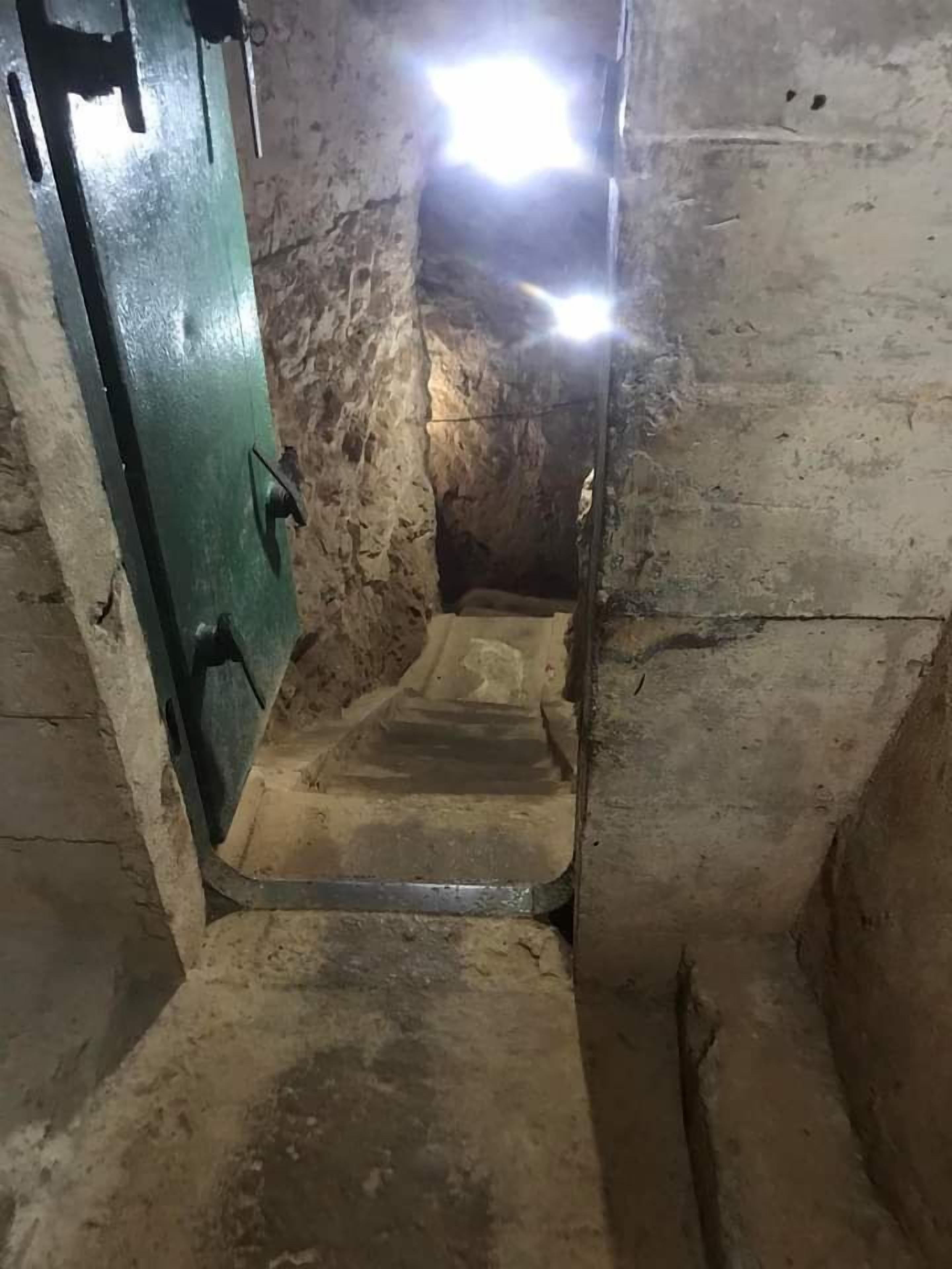A narrow, dimly lit stairway leading to a higher level, with rough stone walls and a metal door on the left.