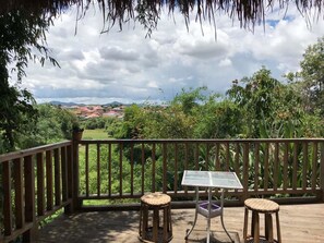A wooden deck with a table and two stools, overlooking a lush landscape with trees and distant hills. - Pukyo Bed and Breakfast (Phonsavan)