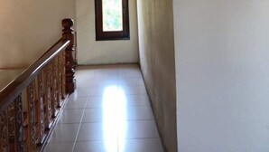 Un corridoio con soffitto in legno, pavimento piastrellato e una finestra vista su vegetazione.