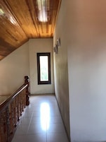 Un pasillo con techo de madera, suelo de baldosas y ventana con vistas a zonas verdes.