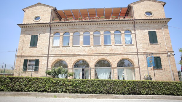 Ein historisches Gebäude mit einer symmetrischen Fassade, Rundbogenfenstern und einem zentralen Balkon mit Blumentöpfen.