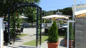 Een poort met een overdekte patio, buitenmeubilair en zicht op geparkeerde auto's en gebouwen op de achtergrond.