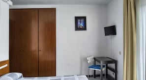 Una habitación de hotel con un armario de madera, un escritorio pequeño con una silla, un televisor y una cama.