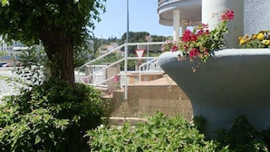 Een gebouw met een witte gevel, een trap die naar een balkon leidt, en een bloempot met roze bloemen.