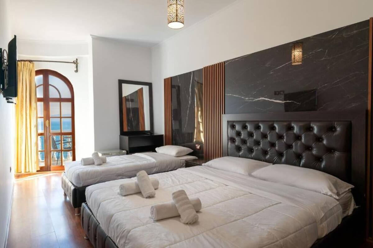 Habitación de hotel con dos camas, un espejo grande, una pared decorativa de mármol y vistas a través de un arco.