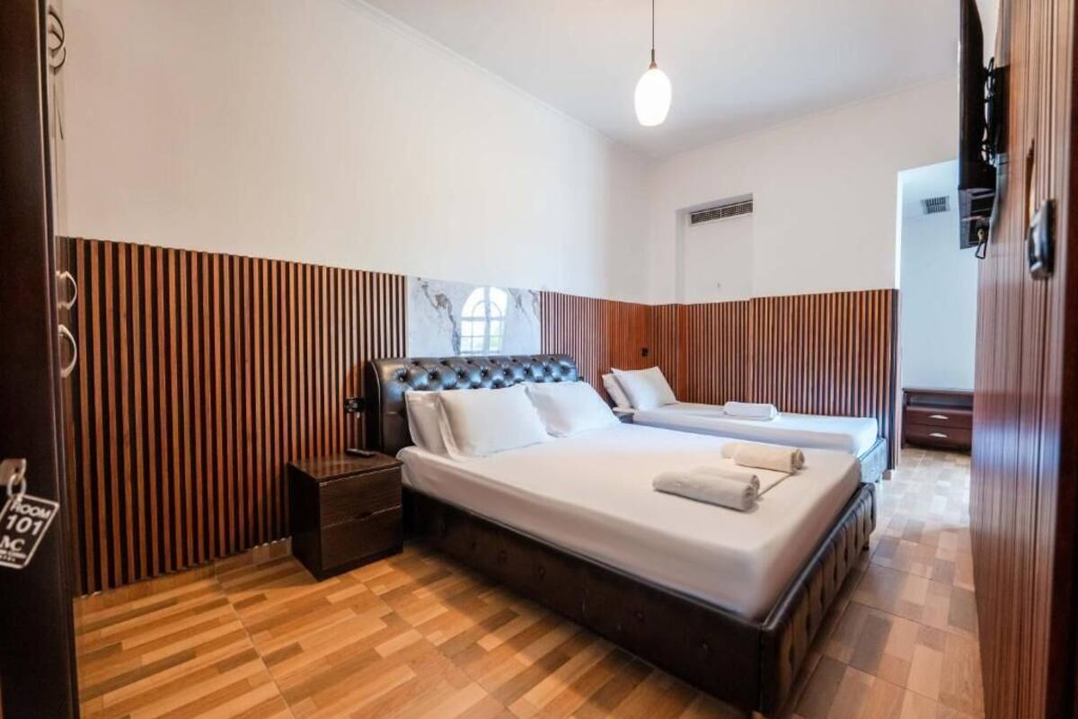 Habitación de hotel con una cama grande, una cama más pequeña, una mesita de noche, un aparador y una ventana con vistas.