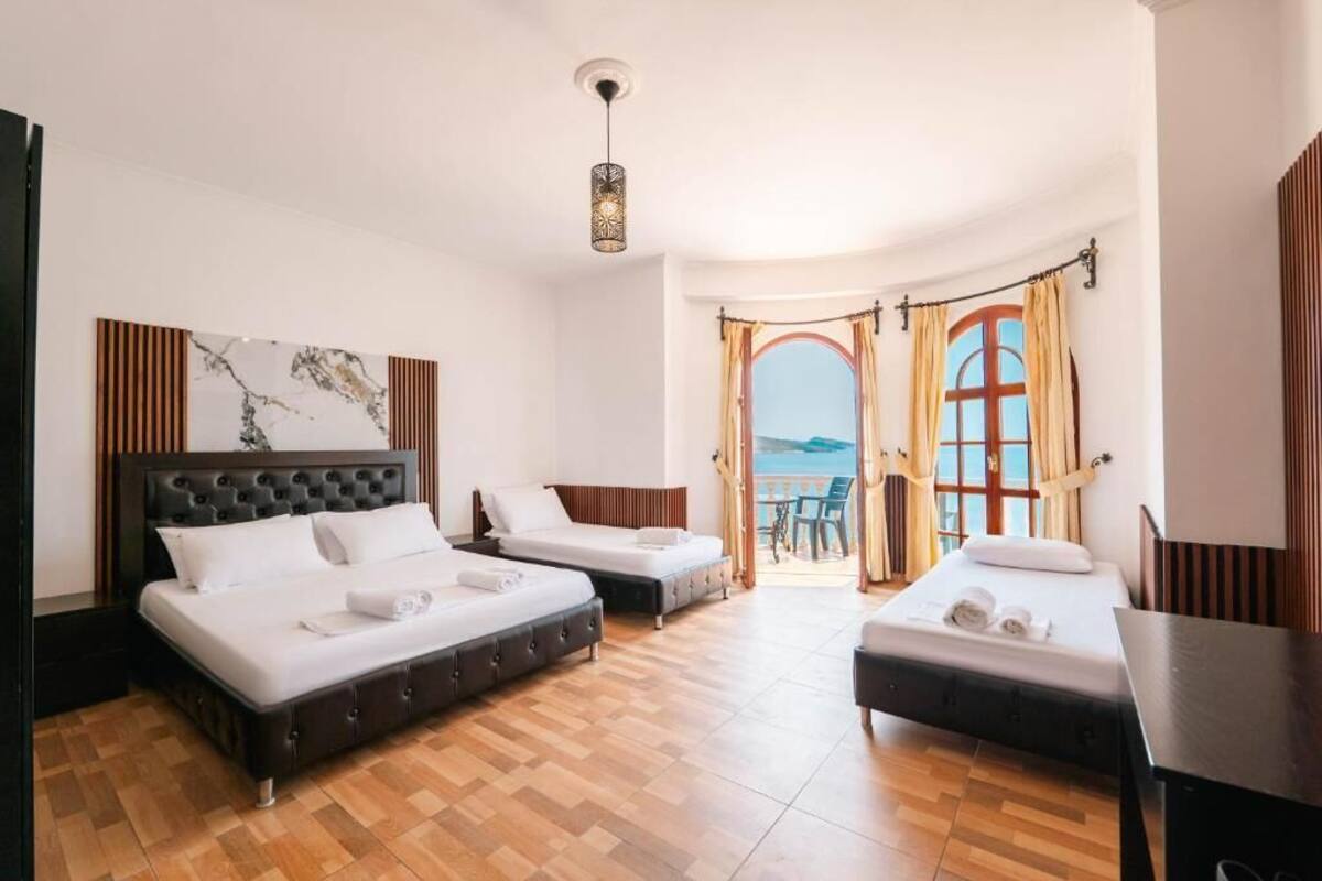 Habitación de hotel con dos camas, un ventanal con cortinas y vistas al mar, además de una lámpara colgante.