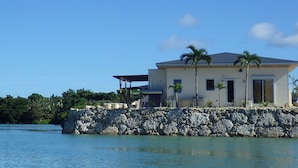 A coastal house with a stone foundation, multiple windows, and a covered porch area. - Lagoon Villa Ryusei (Miyakojima)