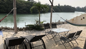 An outdoor seating area with a table and chairs, overlooking a body of water with trees in the background. - Lagoon Villa Ryusei (Miyakojima)