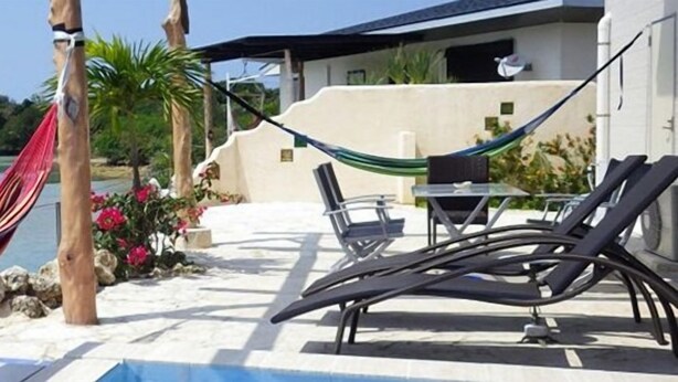 A hammock by a poolside with a view of a calm body of water and greenery in the background. - Lagoon Villa Ryusei (Miyakojima)