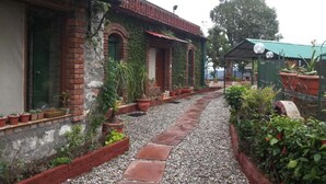 A brick building with a gravel pathway, potted plants, and a small structure with a green roof. - Jharipani Castle (Dehradun)